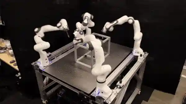 In a lab, four robots move a metal frame using graph neural network coordination on a platform.
