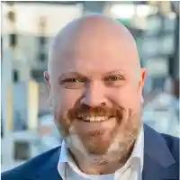 Lars Klippert, Mann mit Glatze und Vollbart. blaues Jacket und weißes Hemd.