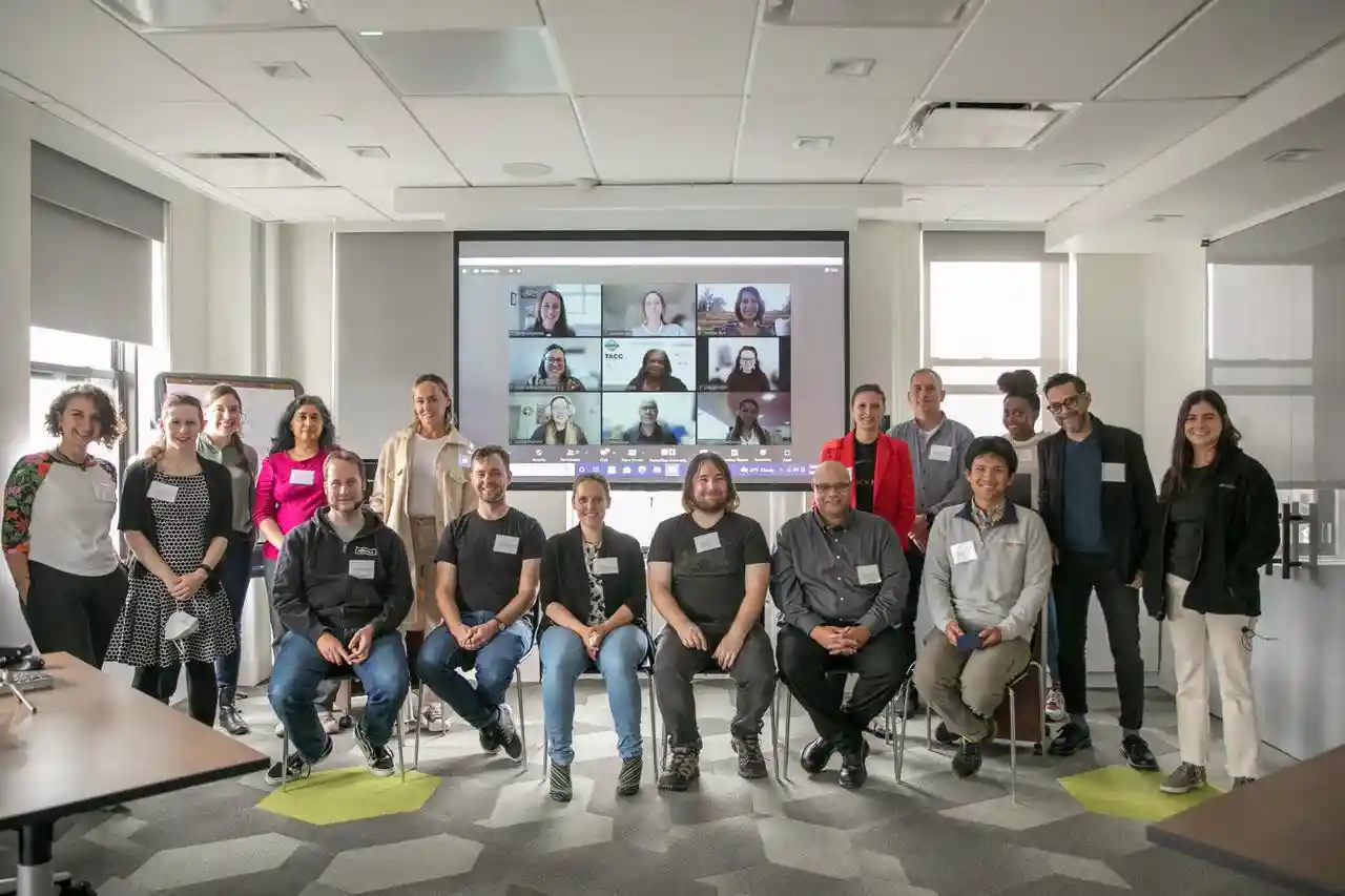 A group of hack the hackathon participants in the room, and on Zoom in the background