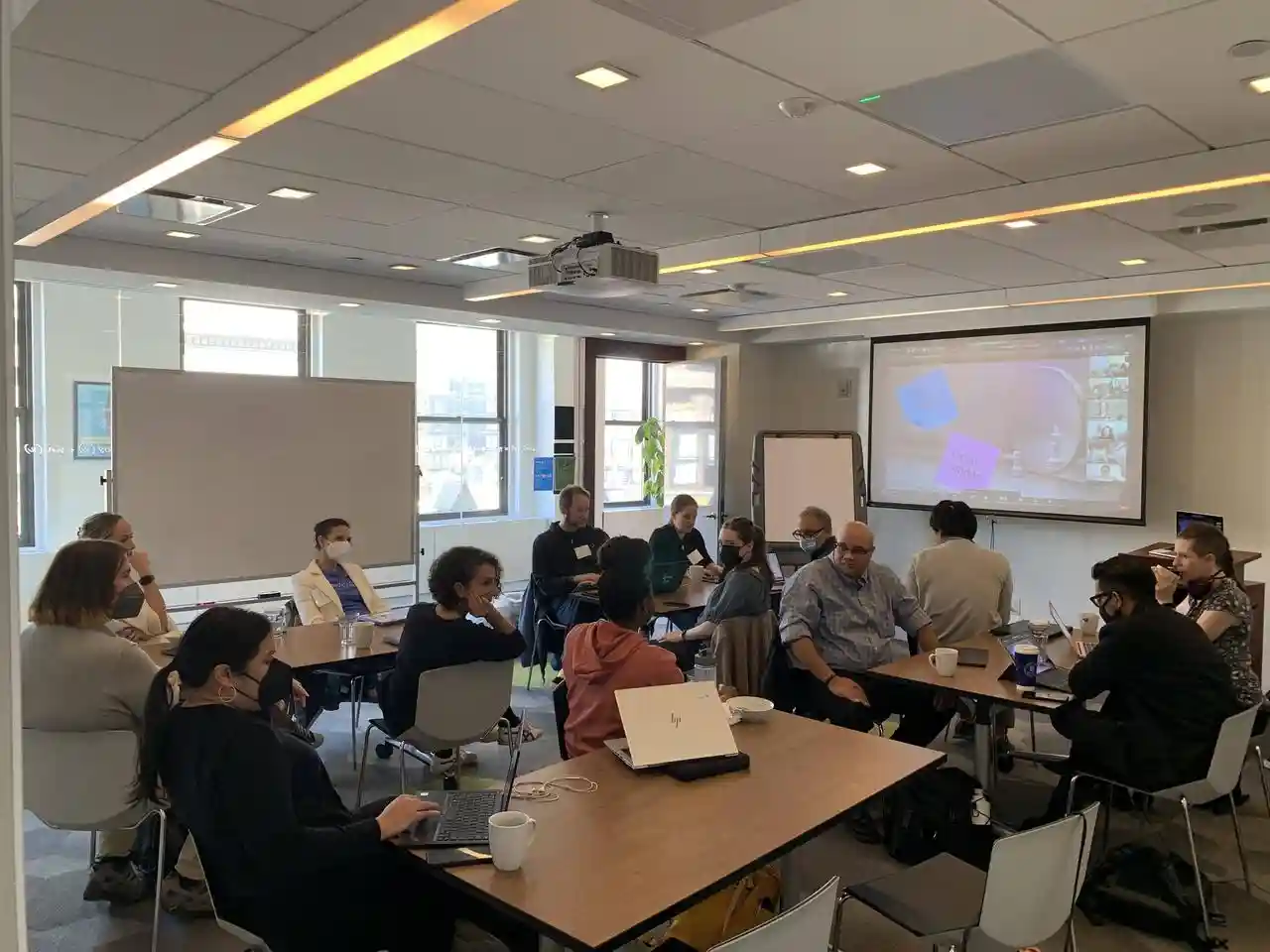 A group of hack the hackathon participants sitting around tables in a meeting room.