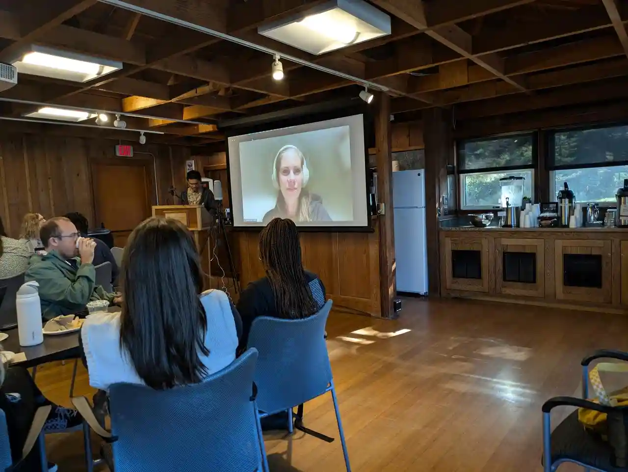 a group of people in a meeting room focused on a person on Zoom during a discussion.