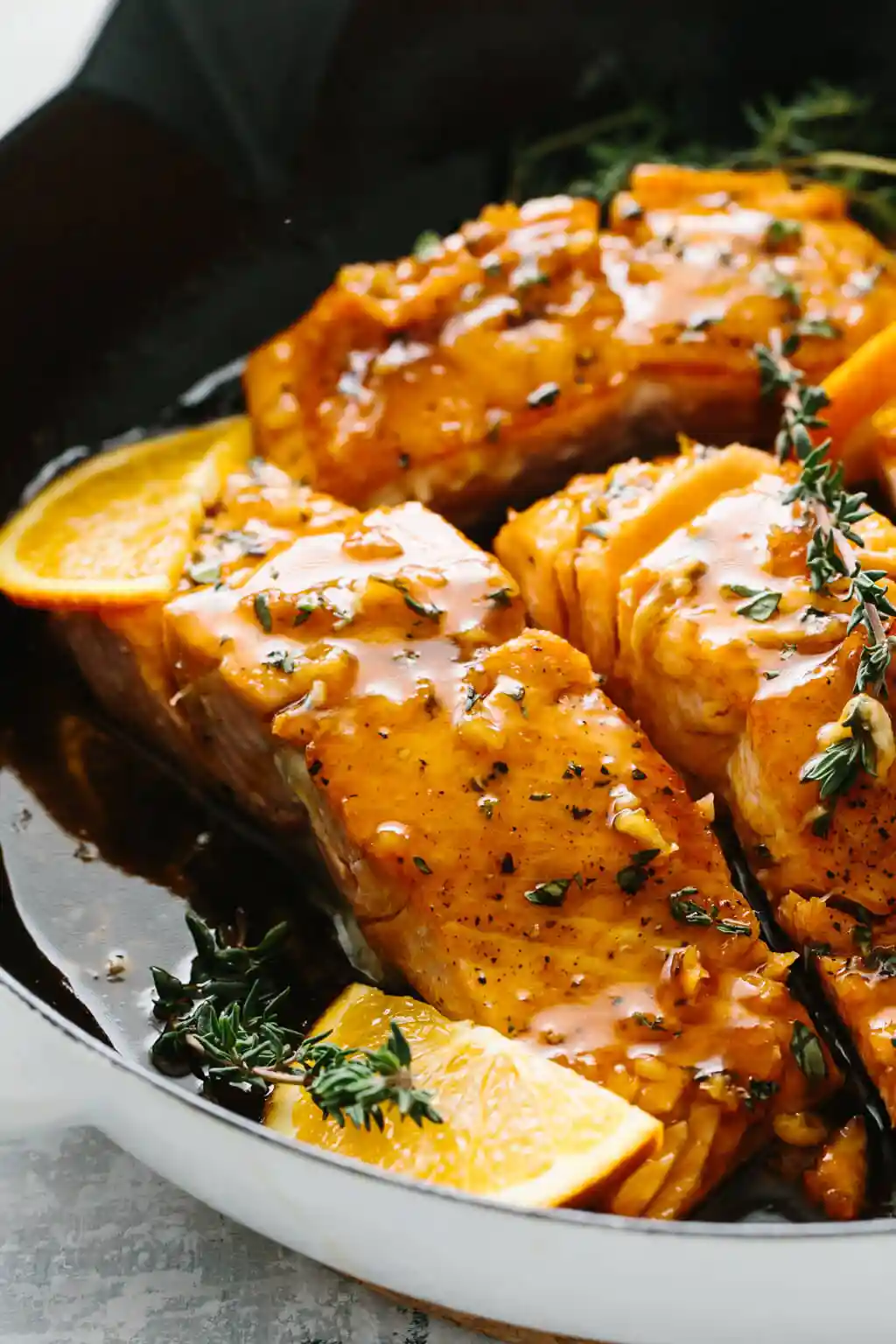 Four salmon filets in a pan with orange slices and thyme on top.