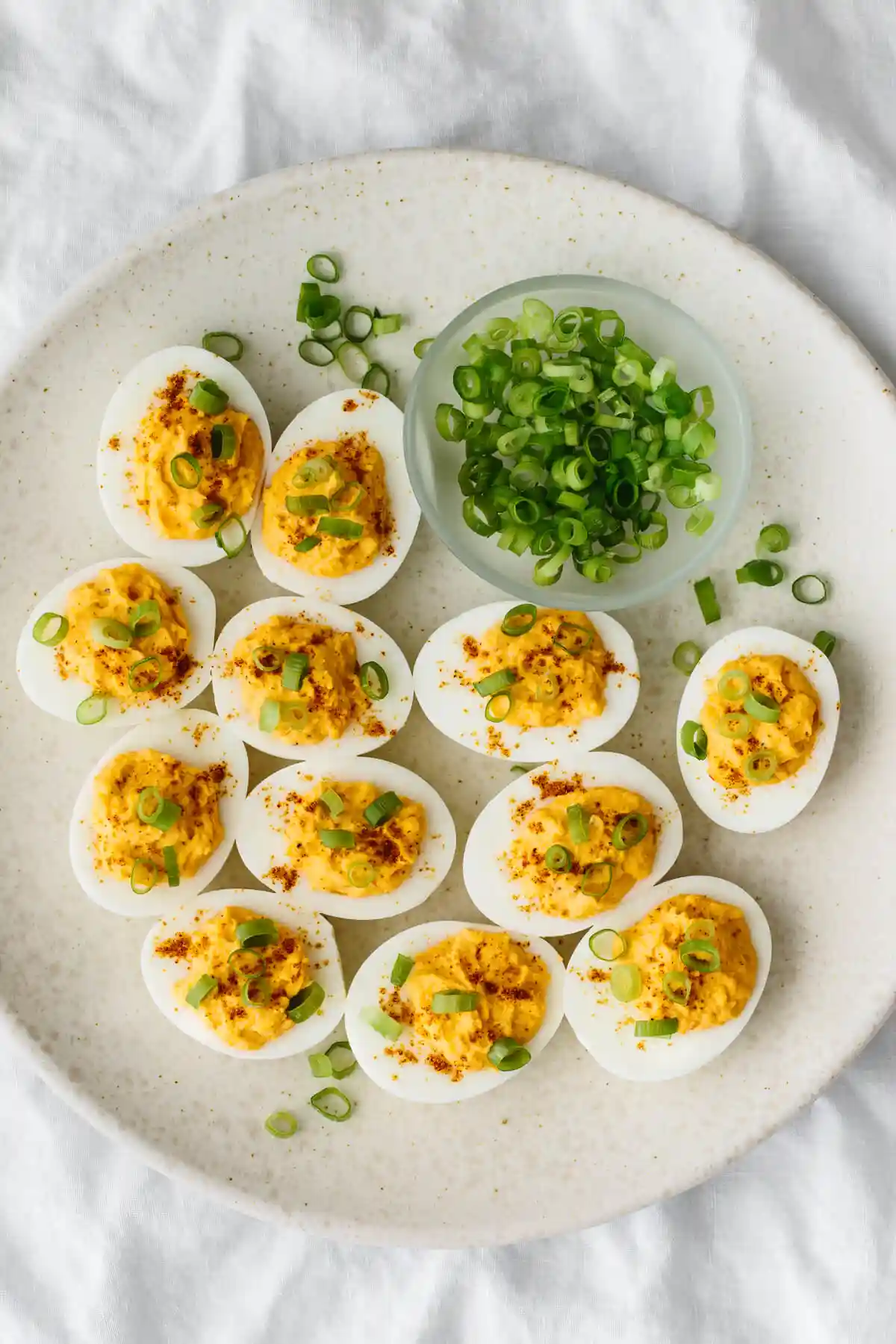 Spicy deviled eggs on a white plate with green onions.