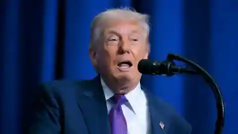 Donald Trump at a lectern with a blue suit, purple tie and US flag pin.