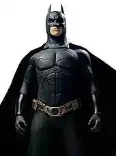 A man in a batsuit, with a cowl on his head, a utility belt, and a cape flowing behind him