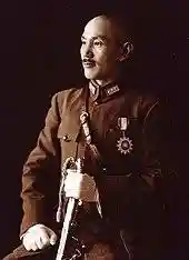 A Chinese man in military uniform, smiling and looking towards the left. He holds a sword in his left hand and has a medal in shape of a sun on his chest.
