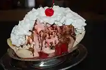 Banana split in a metal dish with vanilla, strawberry and chocolate ice creams topped with whipped cream and a maraschino cherry