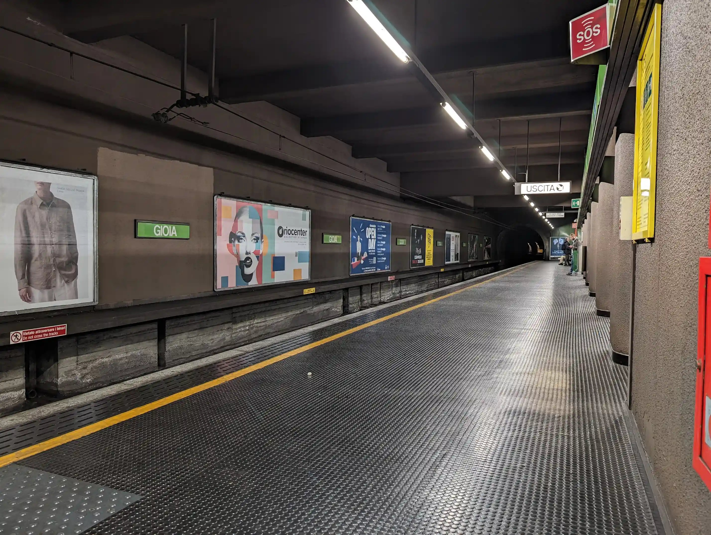 A subway station, with white strip lights lighting the platform and ad posters in the background