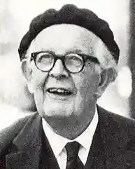 Photo of a man with white hair and glasses, wearing a suit