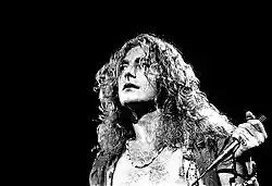 A black and white photograph showing a headshot of Robert Plant with a microphone in hand