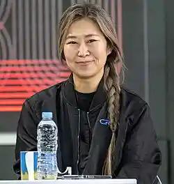 Maggie Kang directly facing the camera while seated at a table