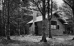 Star Studio in the woods, showing the side with the chimney and the side with a window with curtains